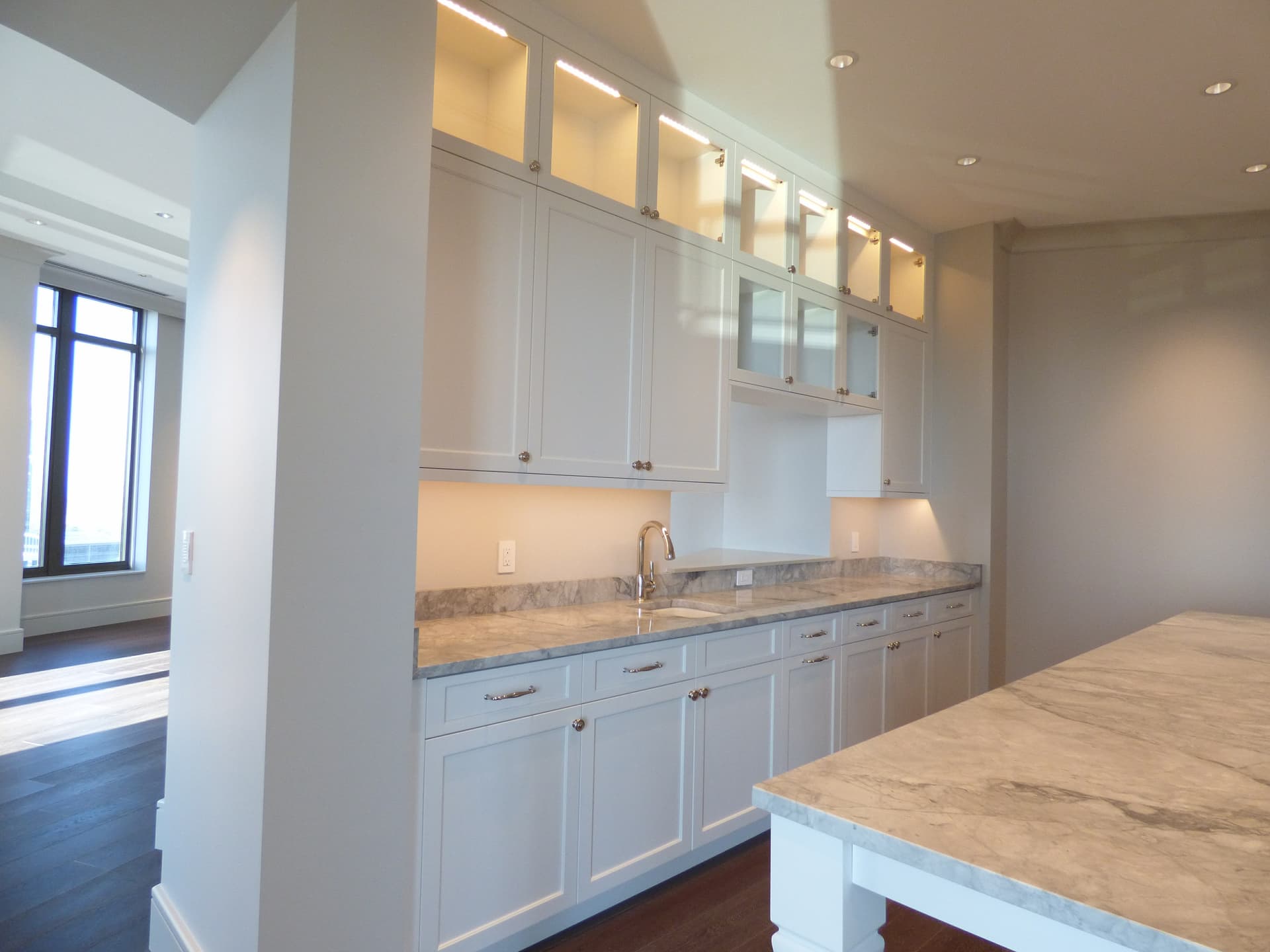 White custom kitchen cabinets with lit glass-front upper cabinets built by Hdez Gabinets