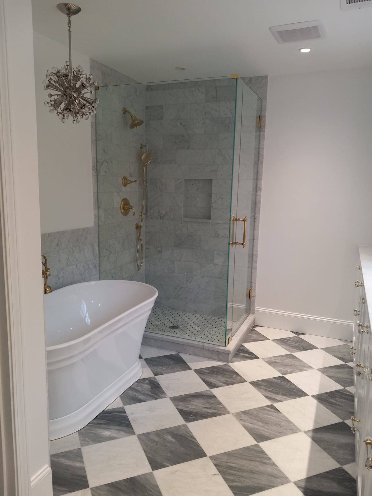 Bathroom with a freestanding tub, glass shower, brass fixtures, and marble checkered floor remodeled by Hdez Gabinets
