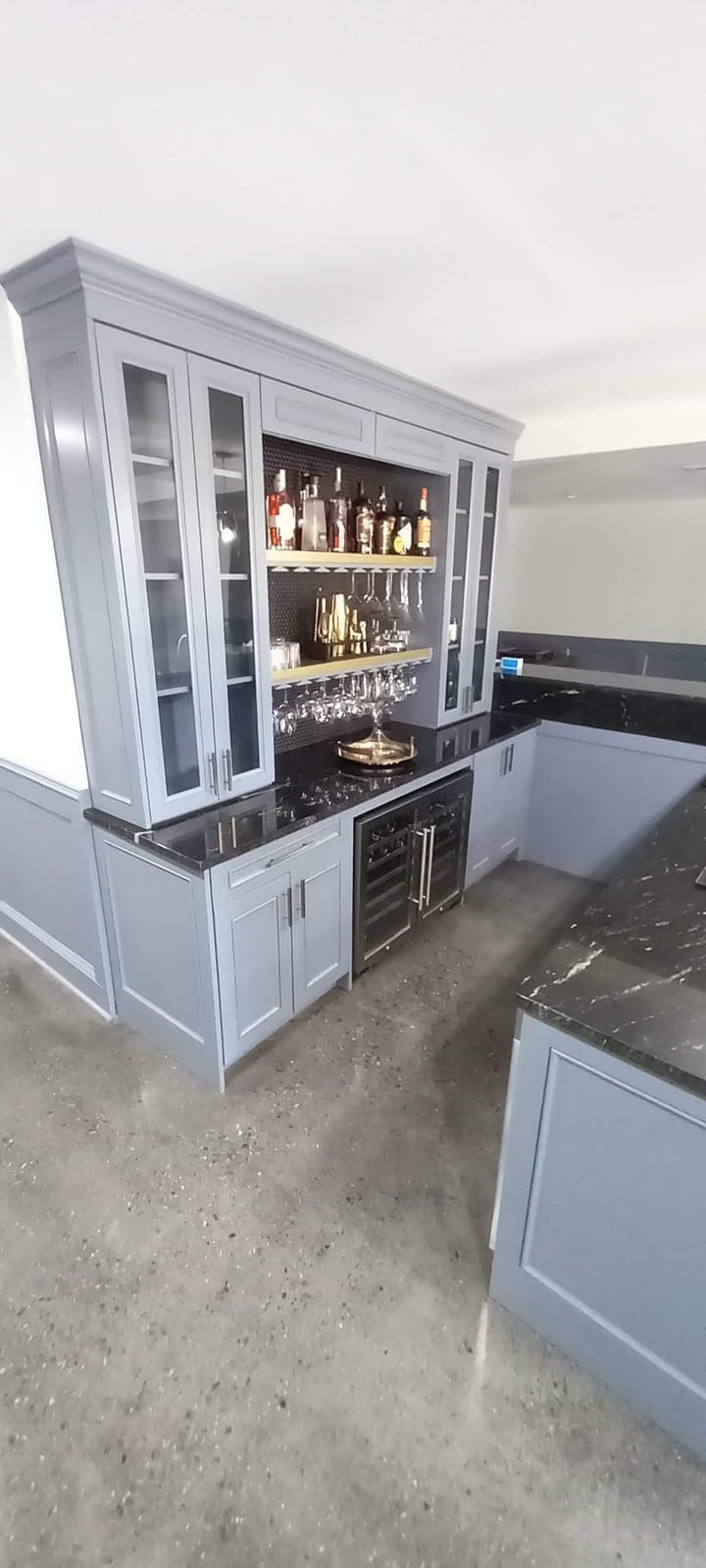 Custom home bar with blue-gray glass-front cabinets and dark stone counters by Hdez Gabinets