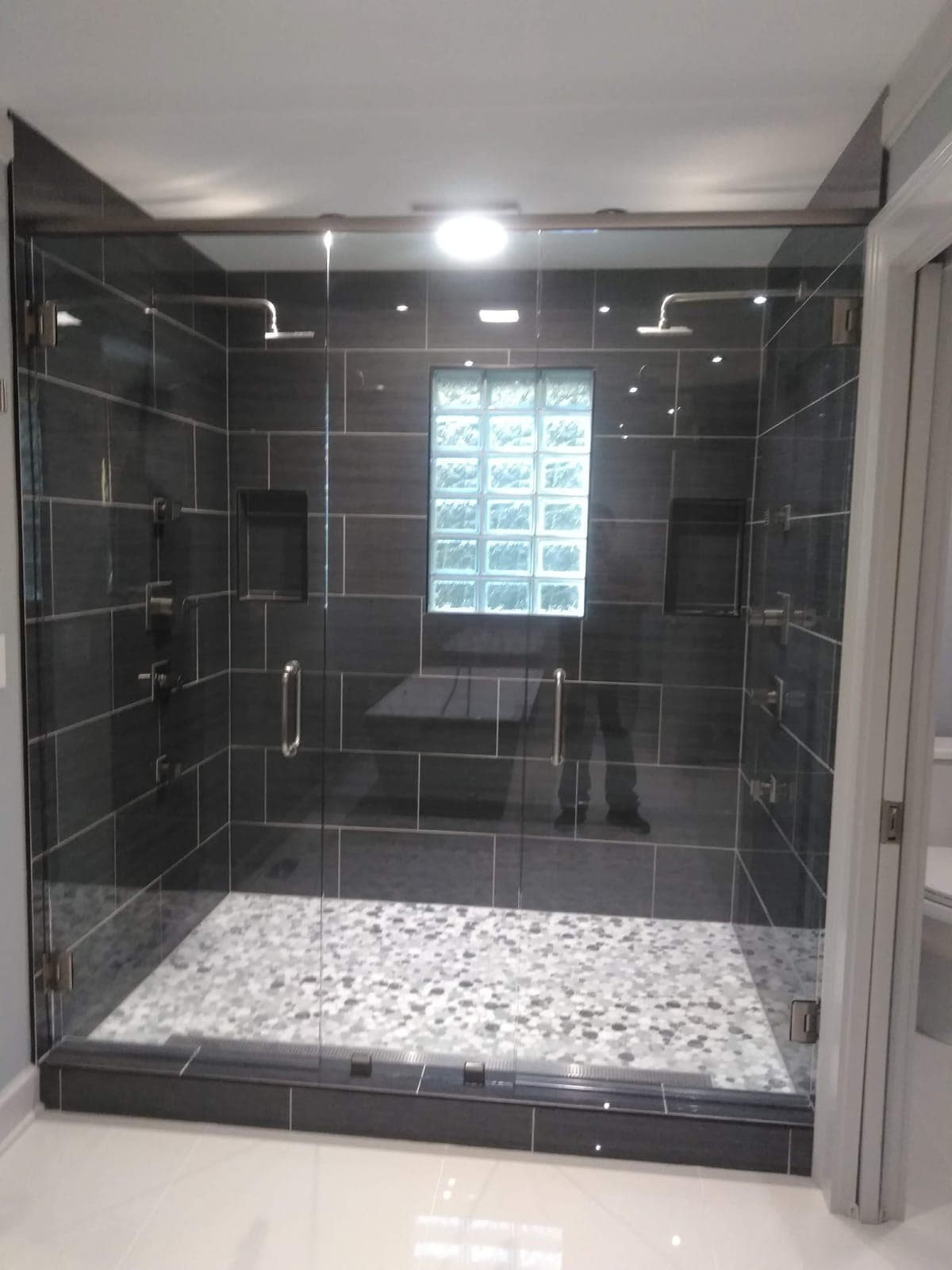 Walk-in shower with dark tile, glass enclosure, and pebble floor by Hdez Gabinets