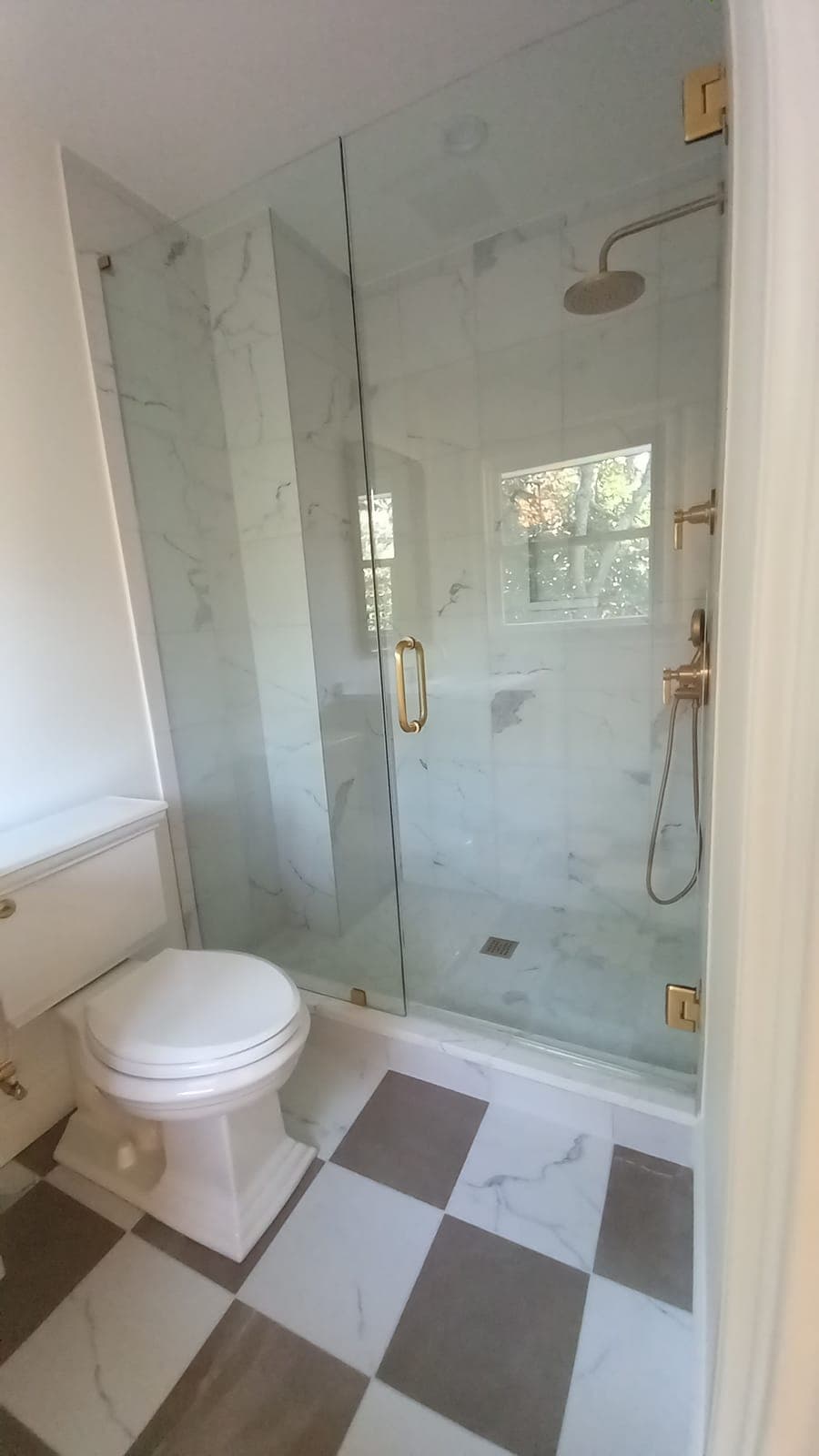 Glass shower enclosure with marble-look tile and gold hardware in a bathroom by Hdez Gabinets
