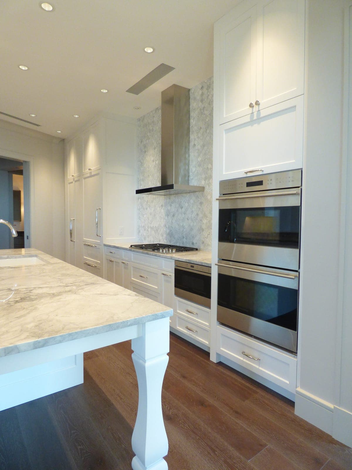 White custom kitchen with double wall ovens, range hood, and a white island built by Hdez Gabinets