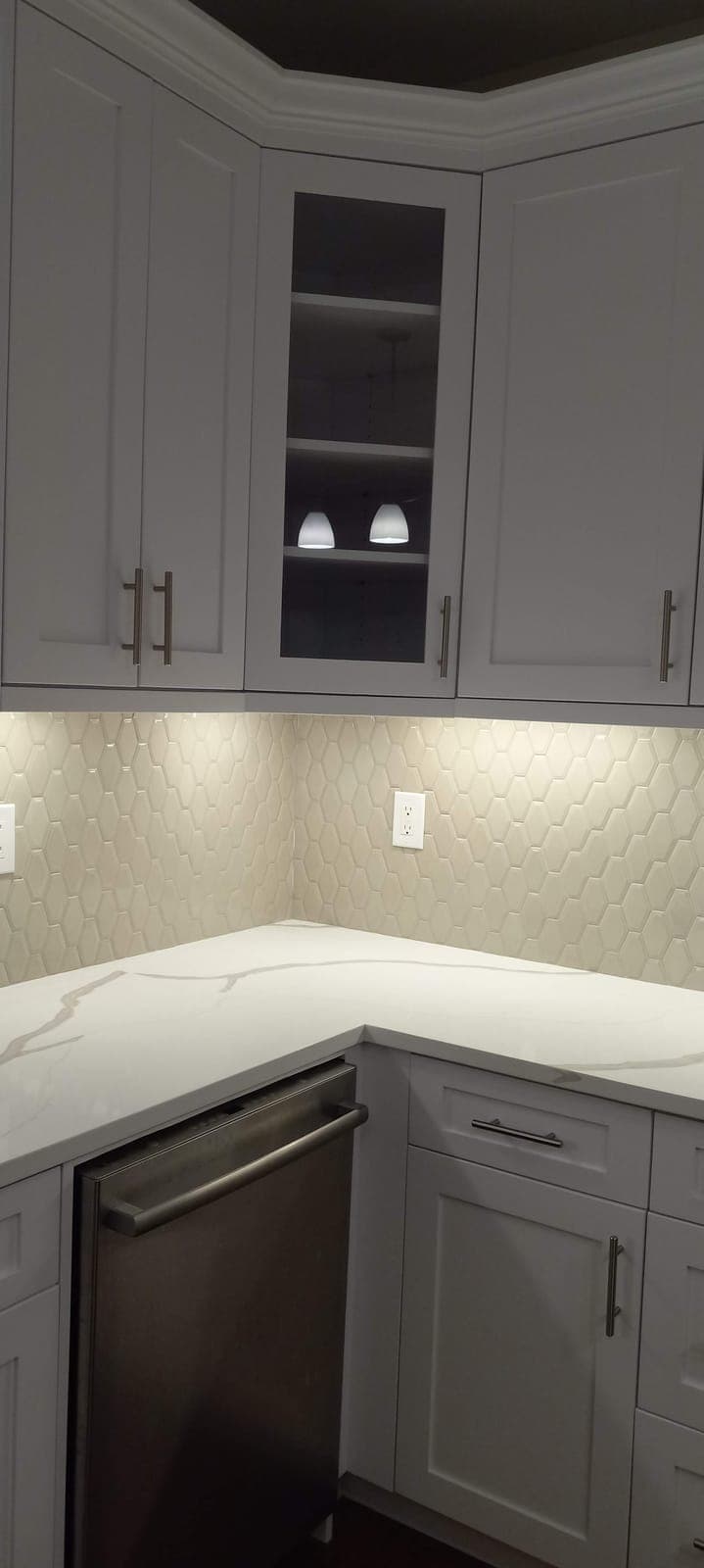 Gray kitchen cabinets with a glass-front upper and diamond tile backsplash by Hdez Gabinets