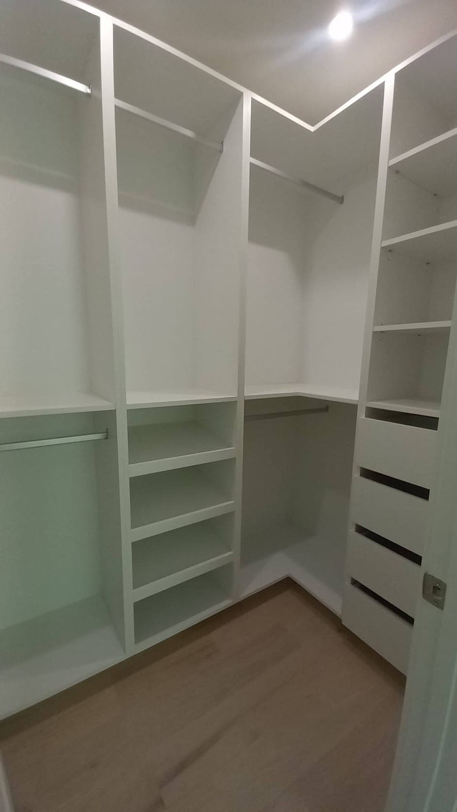 L-shaped walk-in closet with hanging rods, shoe shelves, and drawers built by Hdez Gabinets