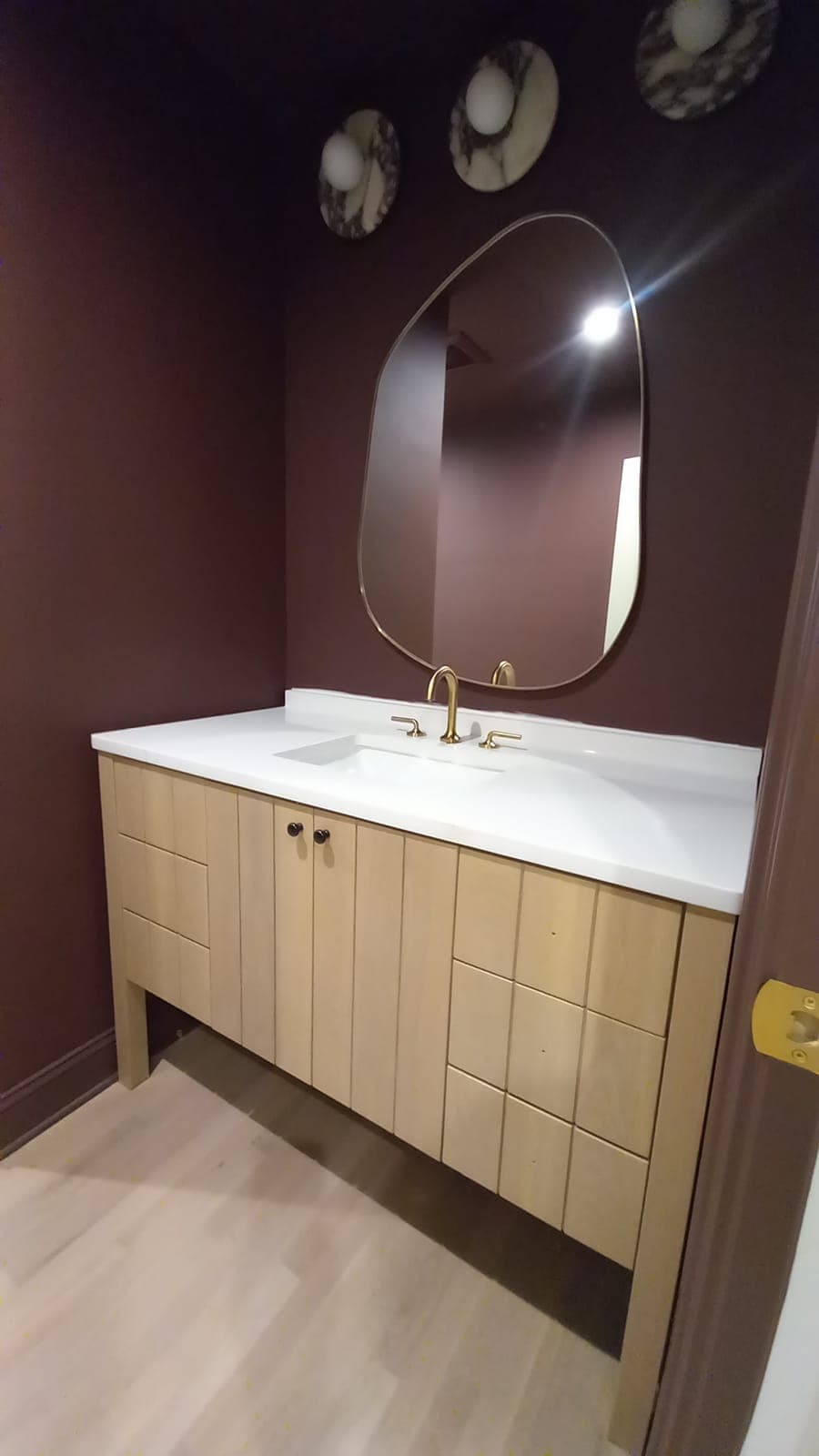 Custom light wood vanity with brass faucet against a plum wall, built by Hdez Gabinets