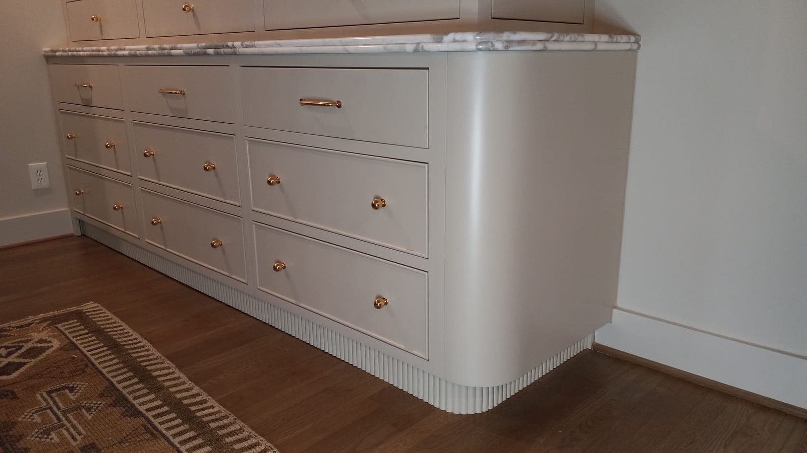 Detail of a rounded fluted cabinet end with drawers and brass pulls, built by Hdez Gabinets