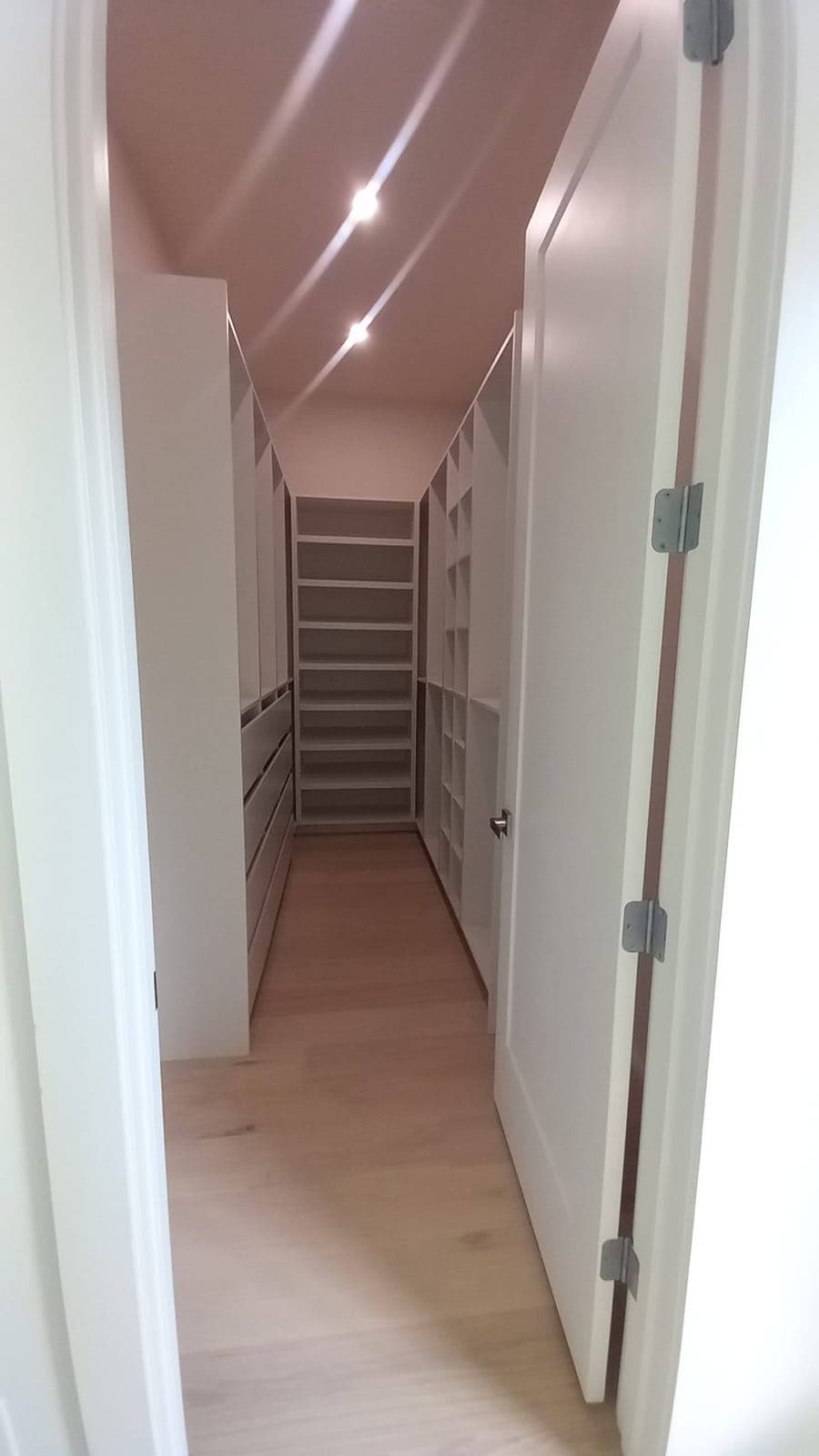 Narrow walk-in closet with white shelving and drawers following a sloped ceiling, built by Hdez Gabinets