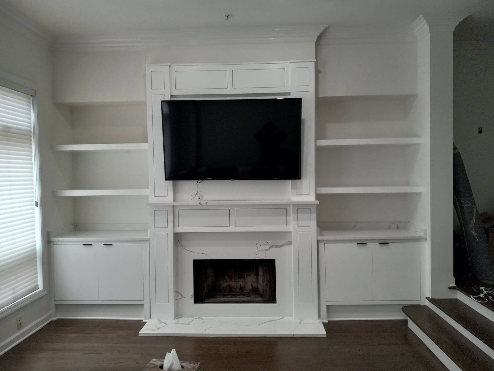 White custom fireplace surround with built-in shelves and cabinets flanking the TV, by Hdez Gabinets