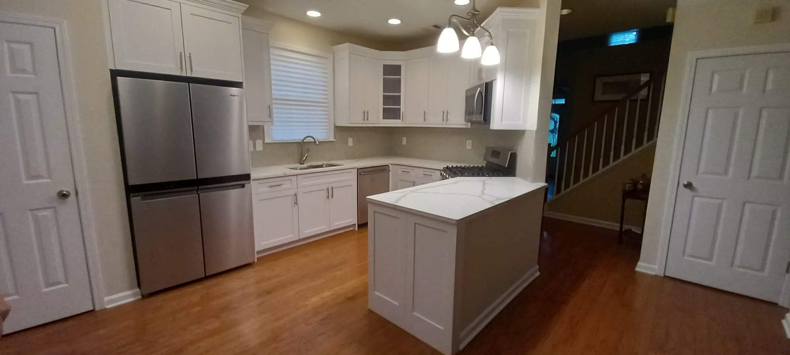 White shaker kitchen cabinets with a quartz-topped island and hardwood floors, built by Hdez Gabinets in Atlanta