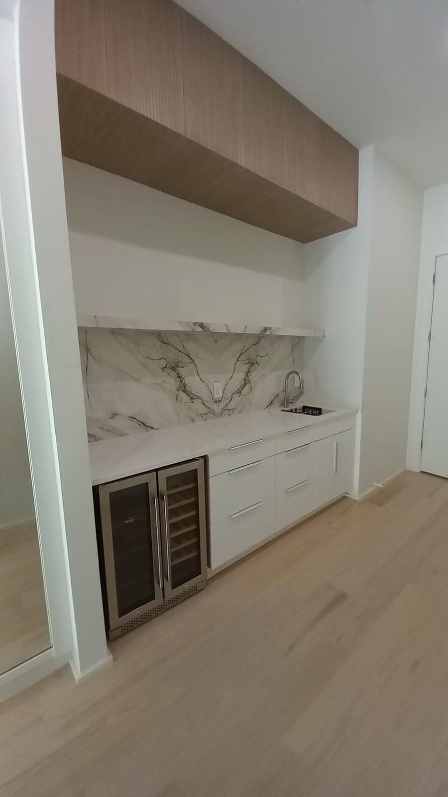 White custom wet bar with a marble backsplash and wine fridge built by Hdez Gabinets
