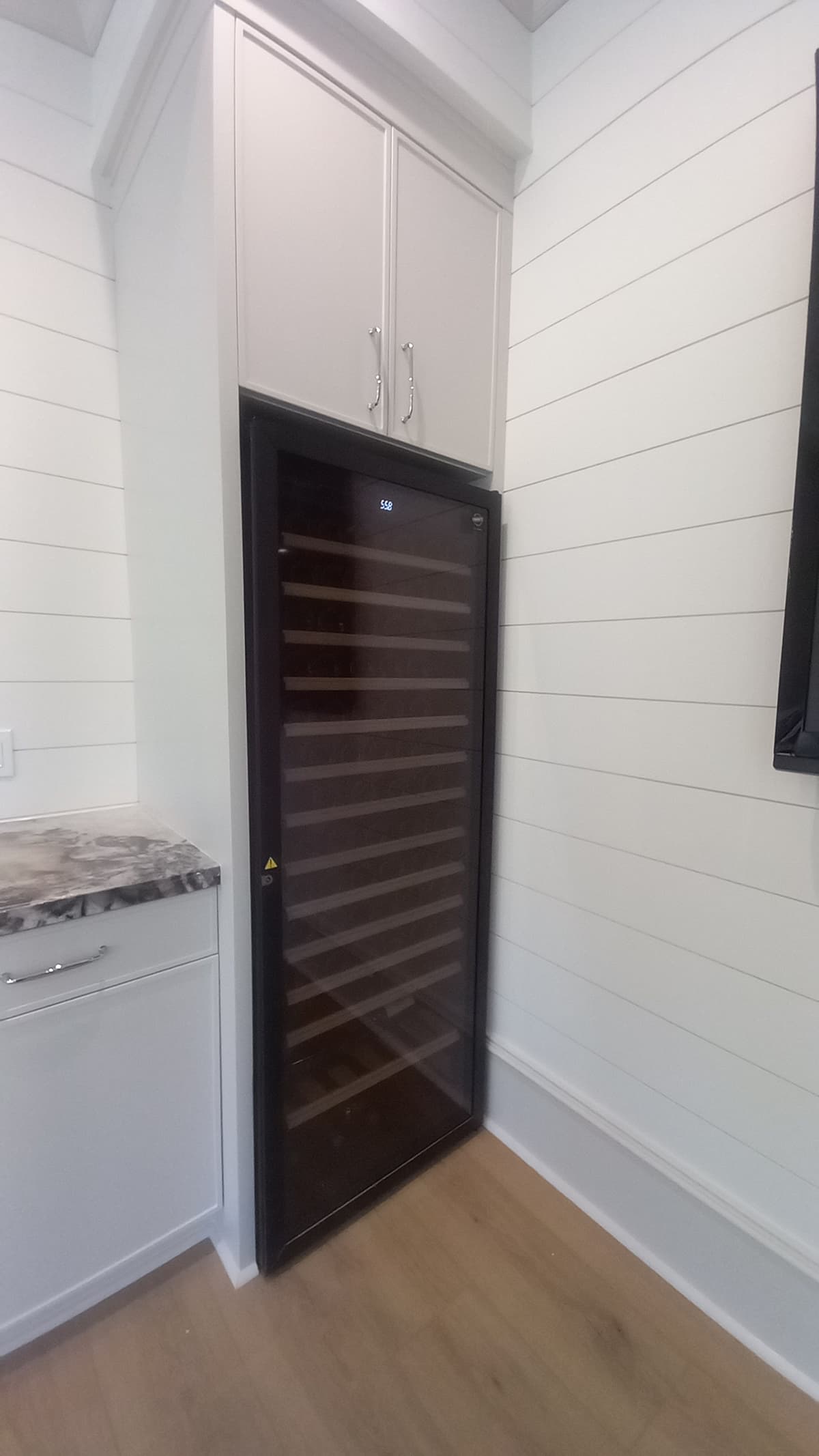Custom built-in cabinet above a wine cooler with a marble counter, built by Hdez Gabinets