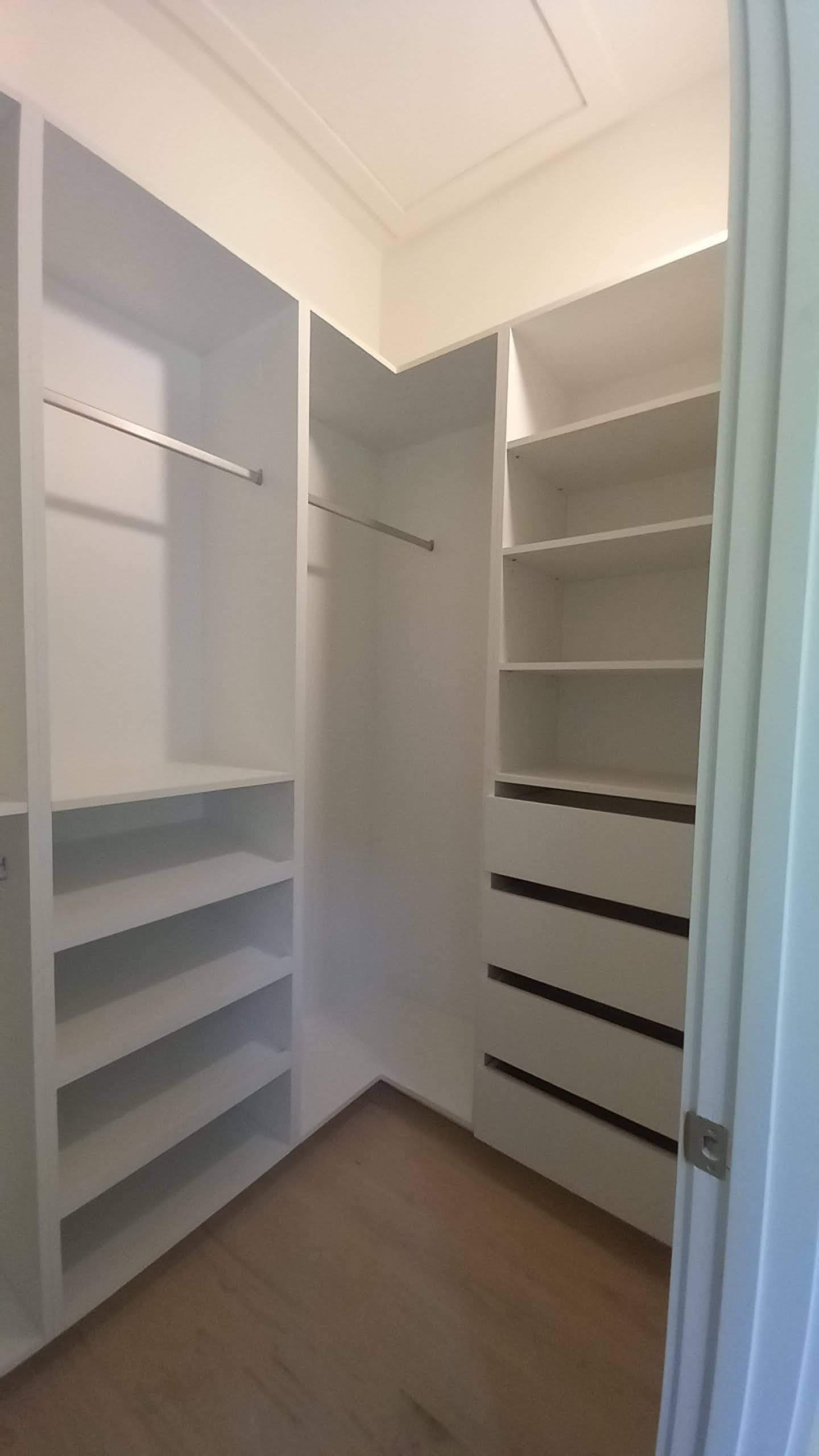 Corner walk-in closet with shoe shelves, hanging space, and a four-drawer bank built by Hdez Gabinets