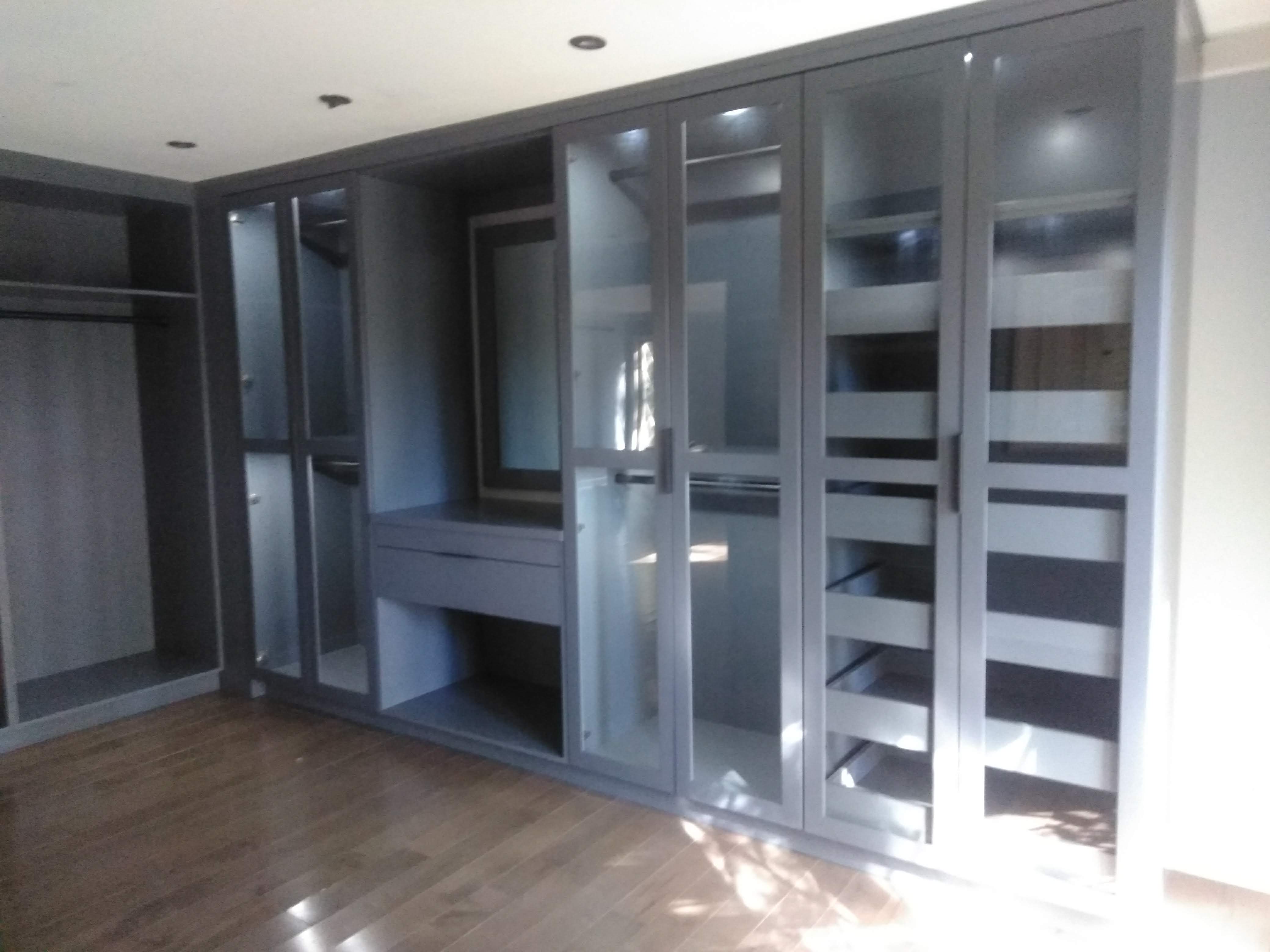 Gray built-in wardrobe with glass-front doors, interior lighting, and pull-out drawers built by Hdez Gabinets in Atlanta