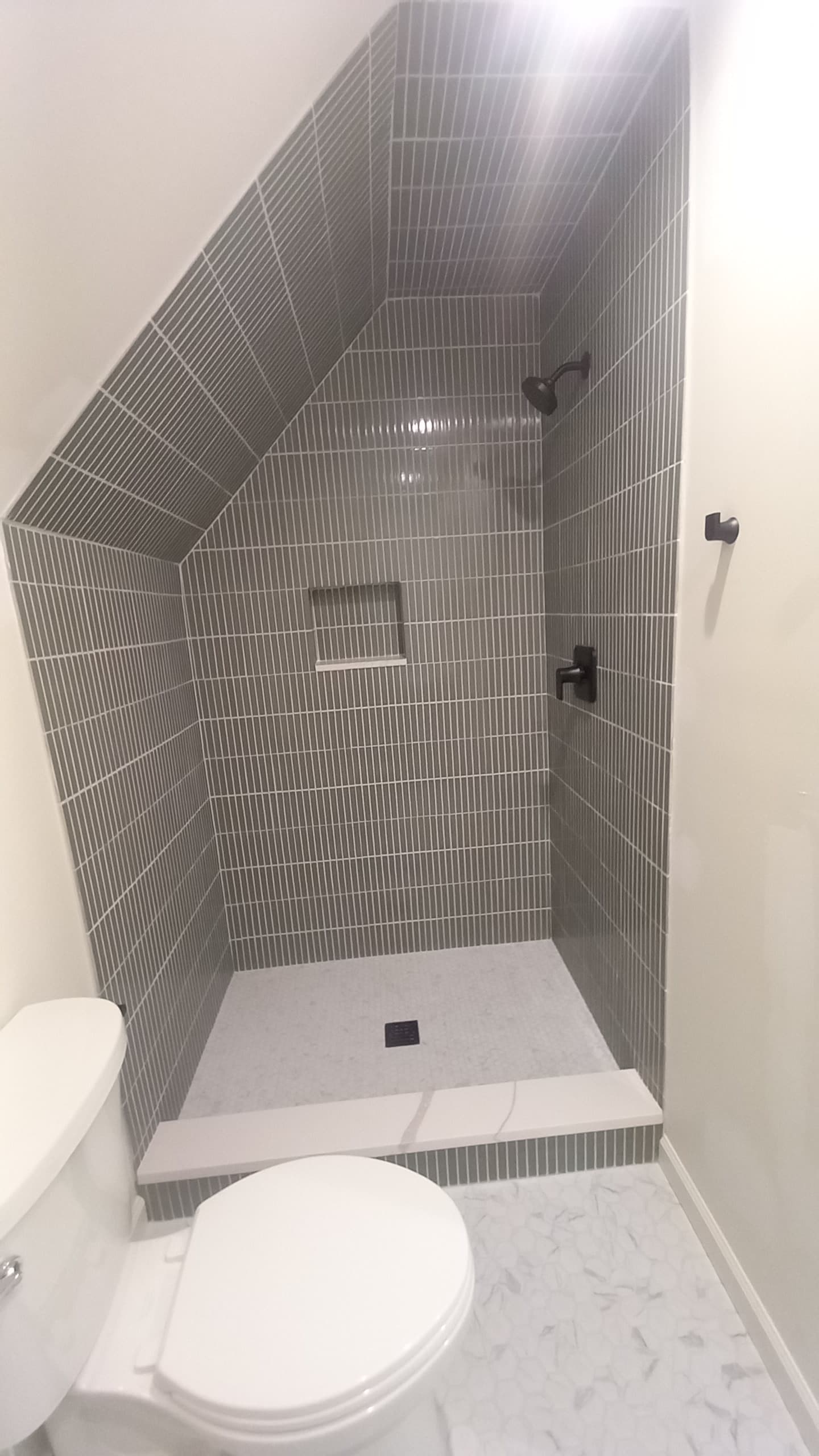 Shower tiled up a slanted ceiling in a small bathroom remodeled by Hdez Gabinets